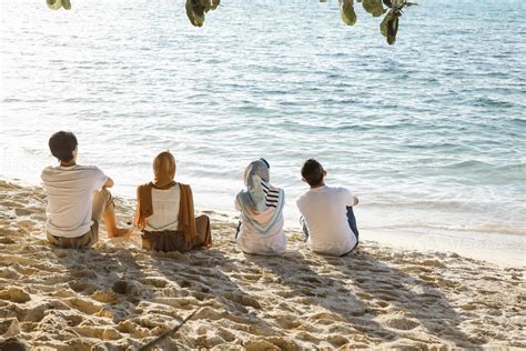 Group Of People Sitting And Relaxing On White Sandy Beach While