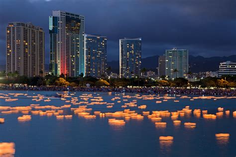 Many Floating Paper Boats Are In The Water Near Tall Buildings At Night