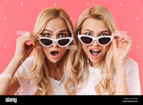 Shocked Blonde Twins Take Off Sunglasses And Looking At The Camera Over Pink Background Stock