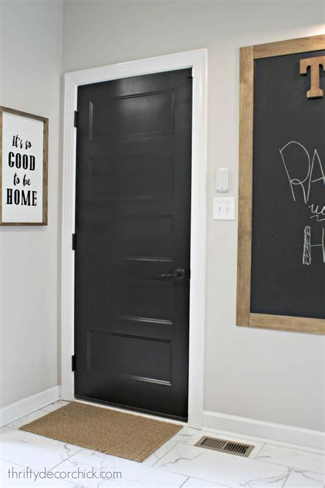 A Black Door In A White Room With A Chalkboard On The Wall Next To It