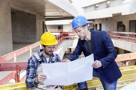 Construction Worker And Architect With Plan Talking On Construction