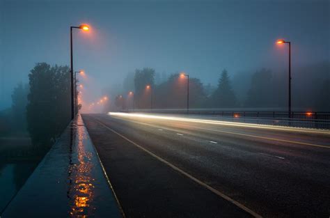 A Foggy Road With Street Lights On The Side