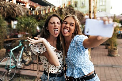 Free Photo Active Young Girls In Stylish Blouses Make Funny Faces Show Tongues And Take Selfie