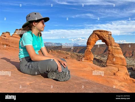 Young Tourist Girl Sitting In Front Of Delicate Arch At Sunset In Utah