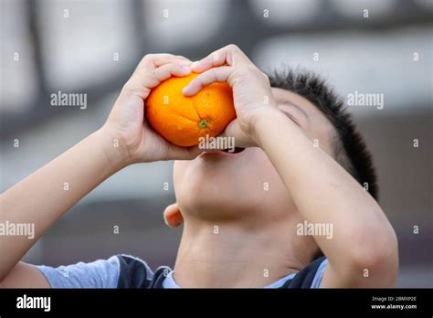 Hand Holding Orange And Squeeze The Juice Into The Mouth Of A Boy Stock