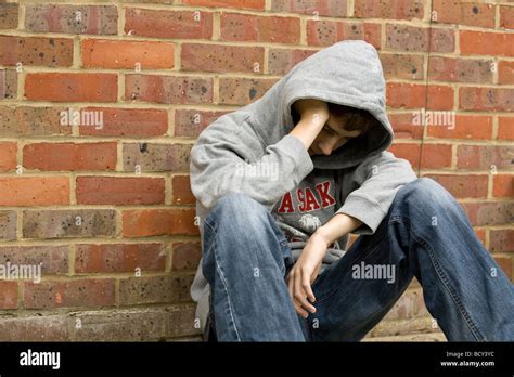Bored Depressed Teenage Boy In Hoodie Sitting Against Brick Wall Stock
