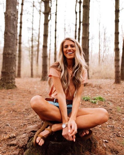 A Woman Sitting On Top Of A Tree Stump In The Woods Smiling At The Camera