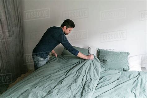 High Angle View Of Man Making Bed While Standing In Bedroom At Home