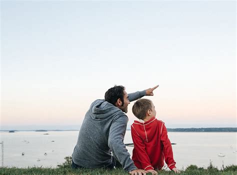 Father Sitting Together With Son Pointing Into The Sky By Stocksy
