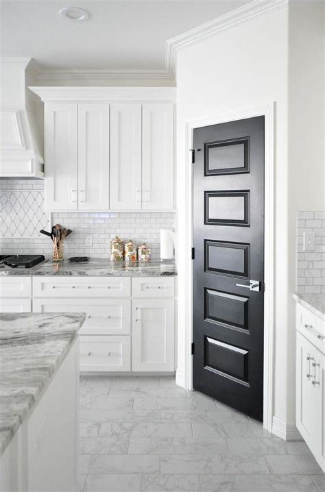 A Black Pantry Door In An All White Shaker Cabinet Kitchen With Marble