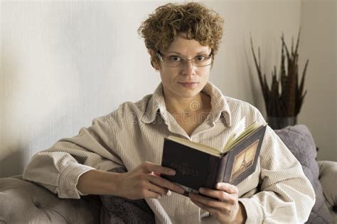 Girl Wearing Glasses Is Sitting On The Couch And Reading A Book Stock