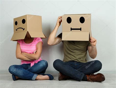Couple With Cardboard Boxes On Their Heads Sitting On Floor Near Wall