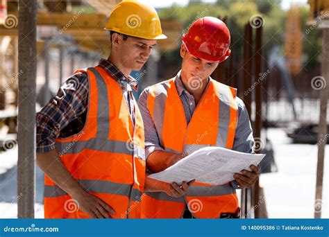 Two Civil Engineers Dressed In Orange Work Vests And Helmets Explore