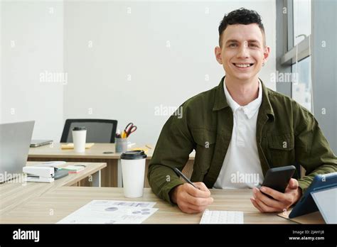 Portrait of cheerful excited young entrepreneur sitting at office desk