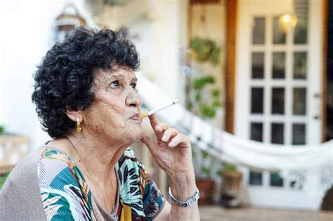 Close Up Of Senior Woman Smoking Cigarette While Sitting Outside House
