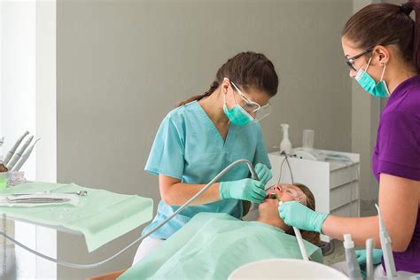 Female Dentist Assisted By Nurse Curing Patient In Her Office By
