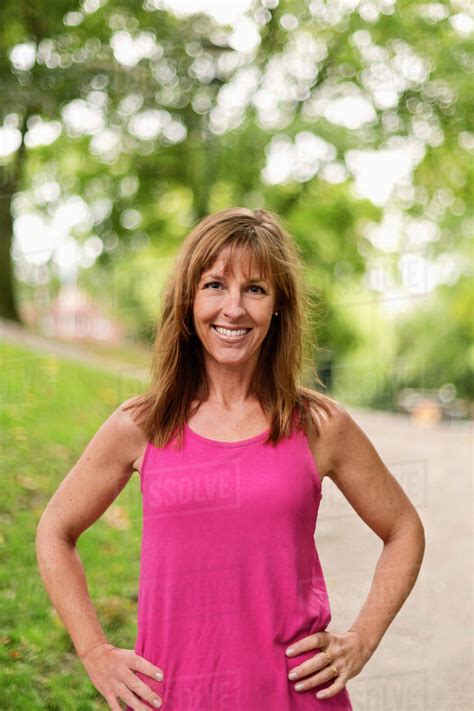 Portrait Of Happy Fit Mature Woman Standing With Hands On Hips At Park