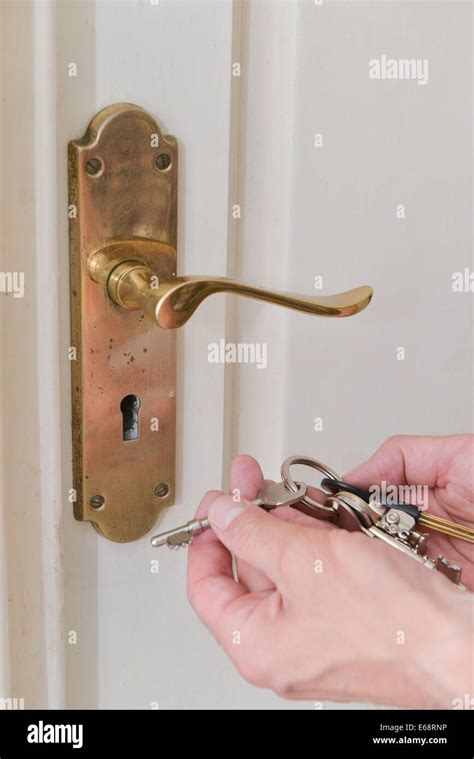 A Mans Hand Holding Bunch Keys In The Lock Of A White Door Stock Photo