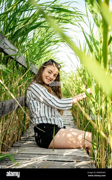 Beautiful Girl Wearing A Striped Shirt Sitting Down On A Wood Path Smiling And Having A Good