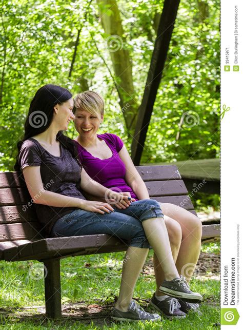Girlfriends Sitting On Park Bench Holding Hands Vertical