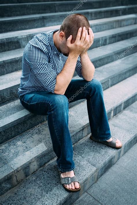 Sad Young Man Covering His Face With Hands Sitting On Stairs Of Big