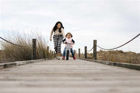 Mother And Daughter With Balance Bicycle On A Boardwalk In The