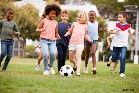 Group Of Children Playing Football With Friends In Park Stock Photo