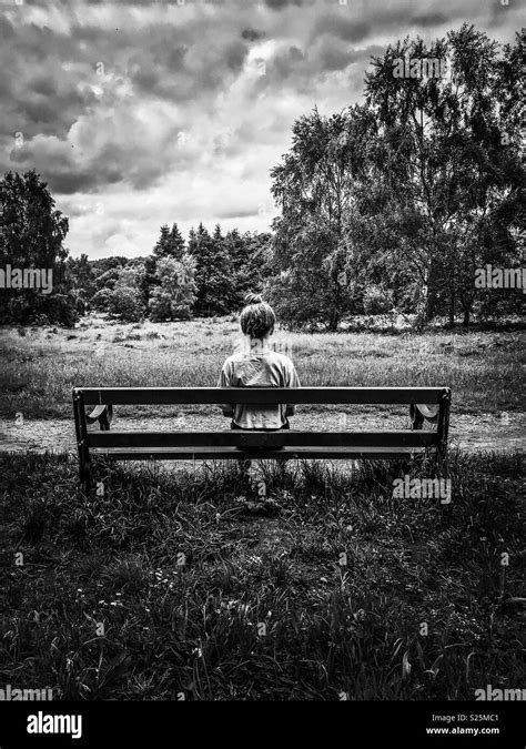 Girl Sitting Alone On A Bench Dark Skies Black And White Stock Photo