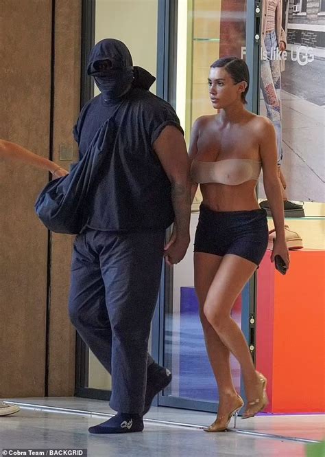 A Man And Woman Walking In Front Of A Store With No Shirt On Wearing