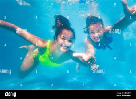 Two Happy Teenage Girls Swim Playing Together Underwater In The Pool
