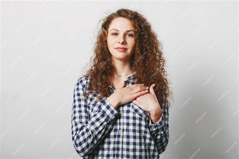 free photo good looking female model with curly bushy hair keeps hand on chest