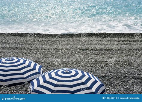 Striped Blue And White Umbrellas On A Pebble Beach On The Promenade Des