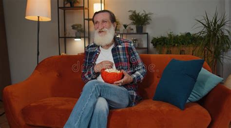 Old Man Sit On Couch Eating Popcorn And Watching Interesting Tv Serial