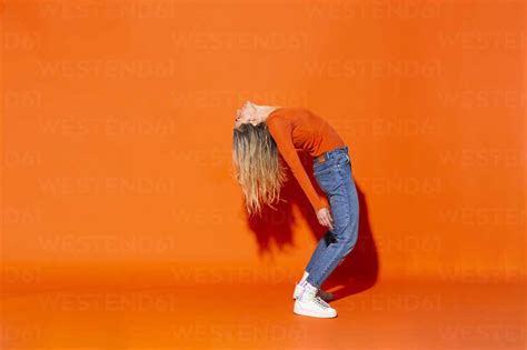 Woman Bending Over Backwards Against Orange Background Stock Photo