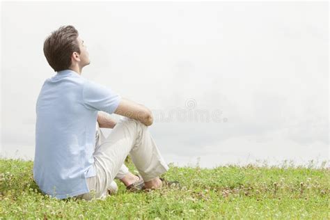 Rear View Of Relaxed Young Man Sitting On Grass Against Sky Stock Image