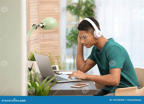 African American Teenage Boy With Headphones Using Laptop At Table