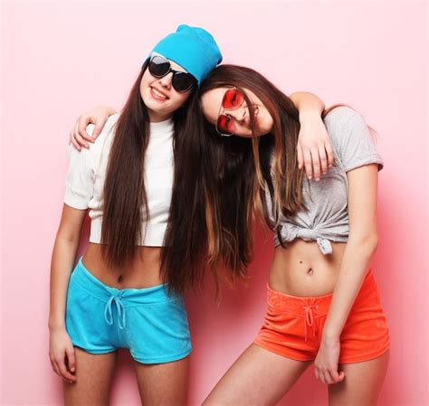 Felices y sonrientes amigas bastante adolescentes abrazándose sobre fondo rosa Foto Premium