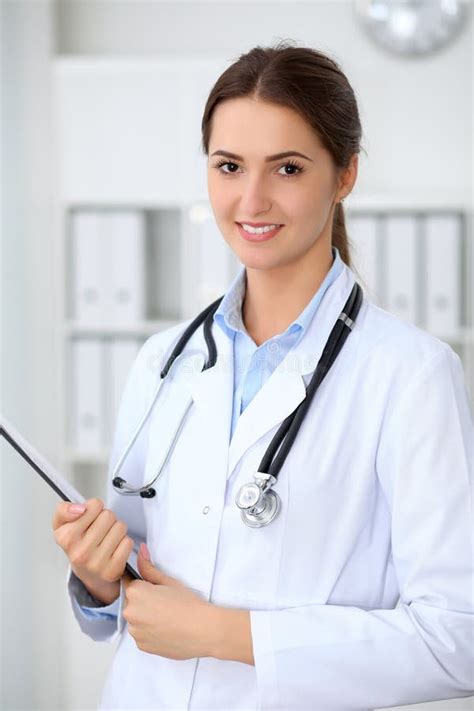 Young Brunette Female Doctor Standing With Clipboard And Smiling At