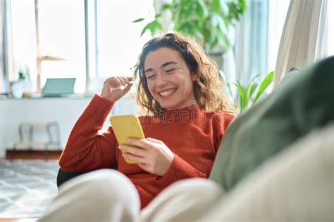 Happy Relaxed Young Woman Sitting On Couch Using Mobile Phone