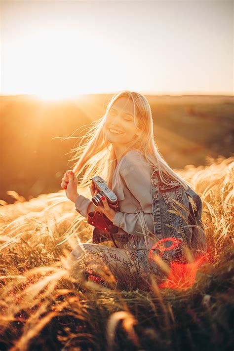 Фото Симпатичная девушка блондинка с фотоаппаратом сидит на поле