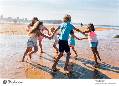 Group Of Six Children Playing Ring A Ring A Roses On The Beach A