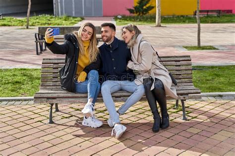 Three Young Smiling Friends Sitting On A Park Bench Two Girls And A