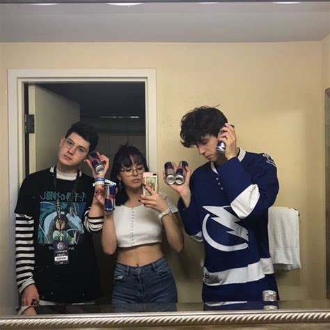 Three People Standing In Front Of A Mirror Holding Up Cell Phones
