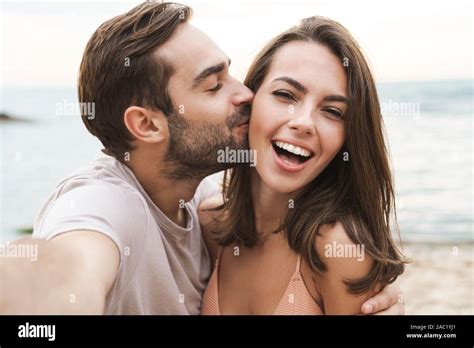 Image Of Young Happy Man Kissing And Hugging Beautiful Woman While Taking Selfie Photo On Sunny