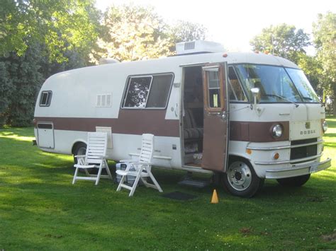 An Rv Parked In The Grass With Chairs Around It