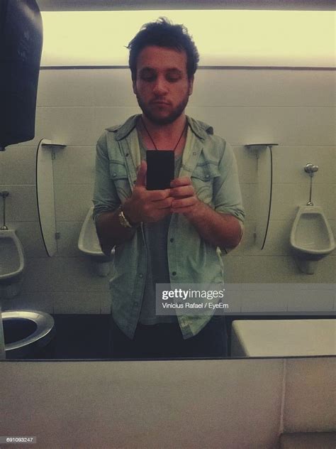 Reflection Of Handsome Man Taking Selfie In Public Restroom On Mirror