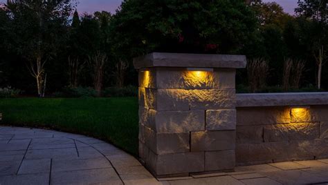 A Stone Wall With Two Lights On It In The Middle Of A Park At Night
