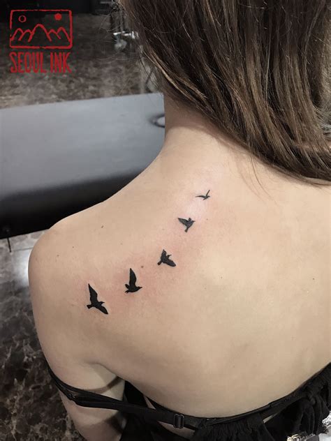 A Small Tattoo Of A Flying Bird Silhouette On The Back Shoulder