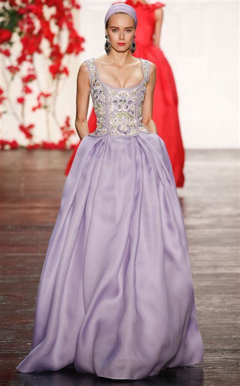 A Woman In A Long Purple Dress Walking Down The Runway With Another