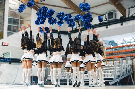 Cheerleaders In Uniform Throwing Blue Pom Poms Up In The Air On A